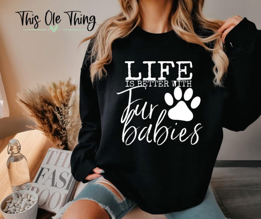 Person wearing a black sweatshirt with 'Life is better with four babies' text and paw print design.