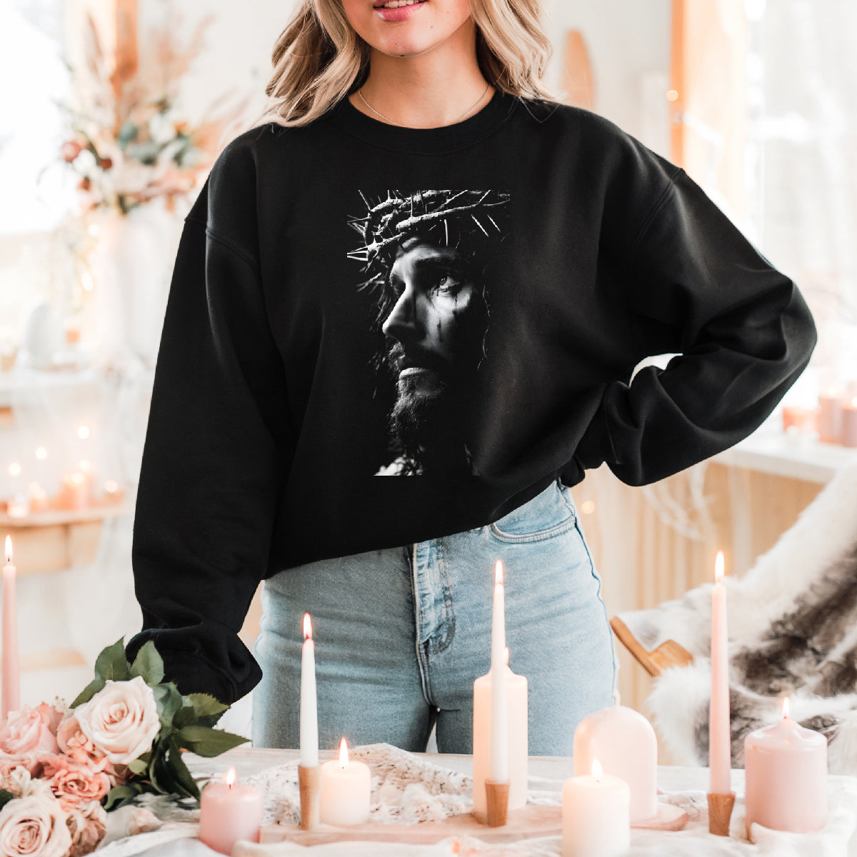 Person wearing a black sweatshirt with a graphic design, standing in a decorated room with candles and flowers.