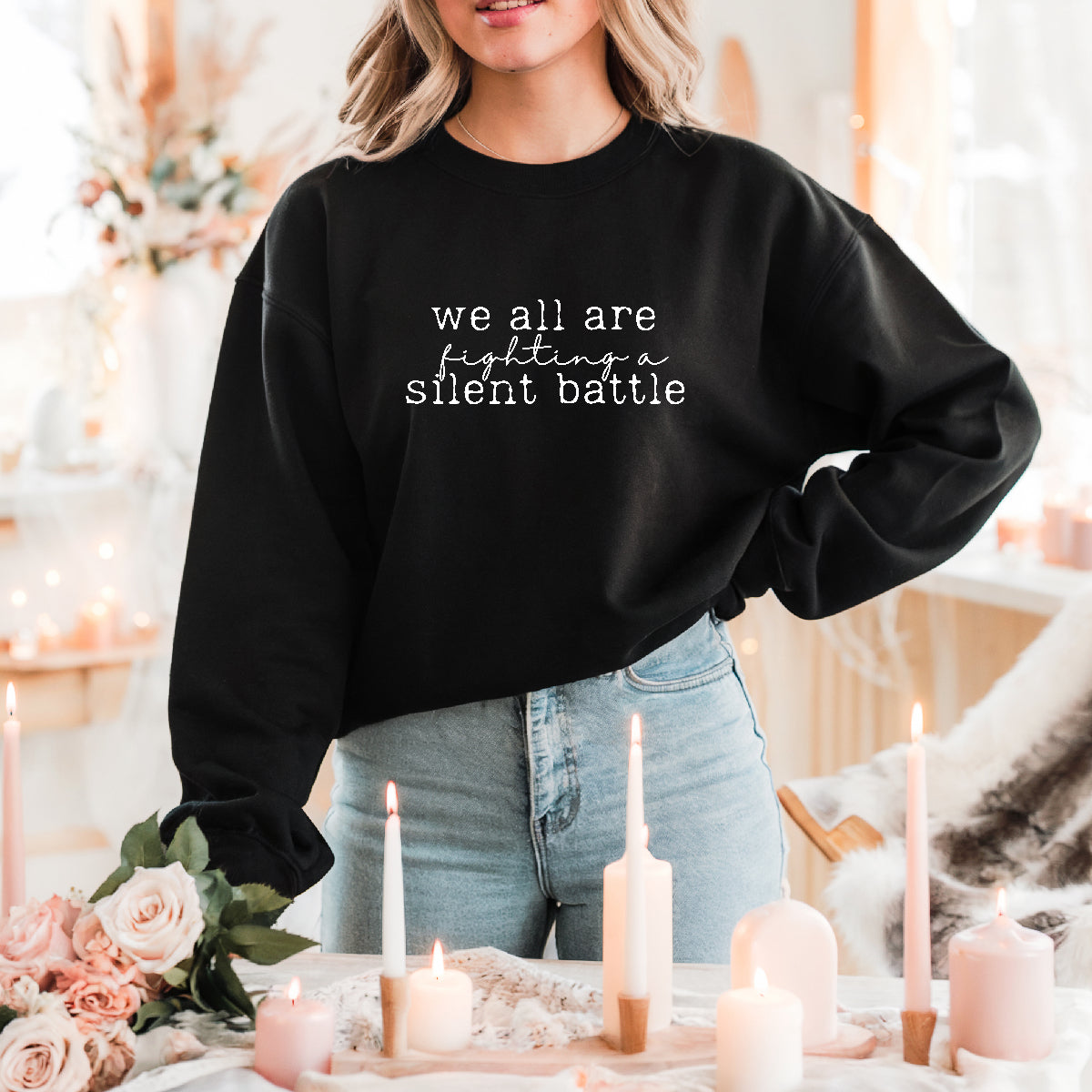 Person wearing a black sweatshirt with text in a cozy indoor setting with candles and flowers.