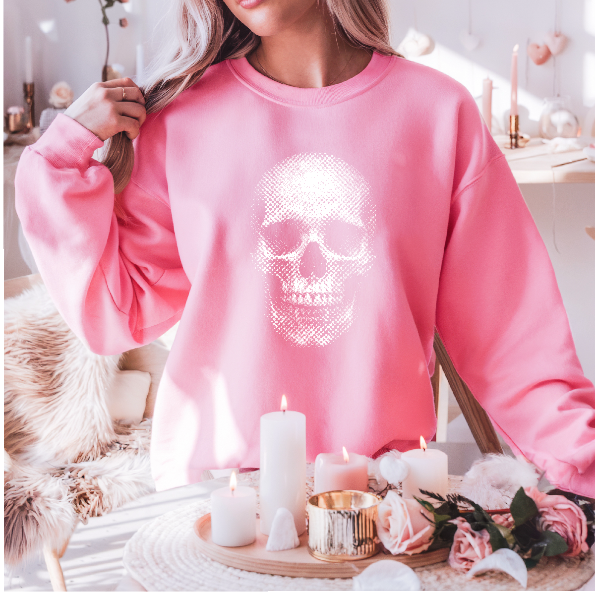 Person wearing a pink sweatshirt with a skull design, standing in a decorated room with candles and flowers.